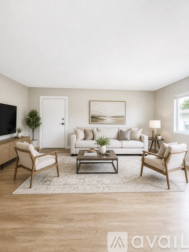 A living room with a white couch, a wooden chair, a glass coffee table, and a television on the wall.