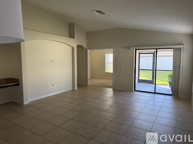 A spacious living room with tiled flooring and a sliding glass door leading to a balcony.