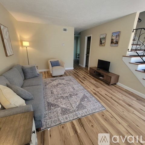 A living room with a grey couch, a white chair, and a rug on the wooden floor.