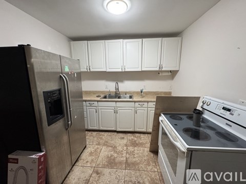 A kitchen with a black fridge, white cabinets, and a stainless steel oven.
