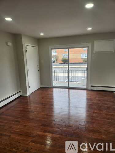 A room with wooden floors and a sliding glass door leading to a balcony.