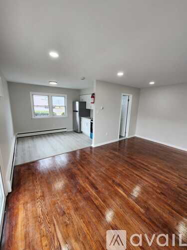A room with wooden flooring and white walls, with a window and a door visible.