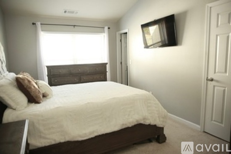 A bedroom with a bed, a window with curtains, and a wall-mounted TV.