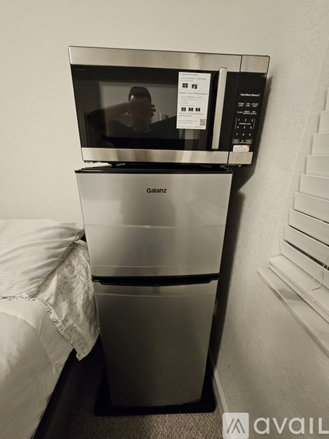 A microwave oven is on top of a stainless steel dishwasher in a small room.