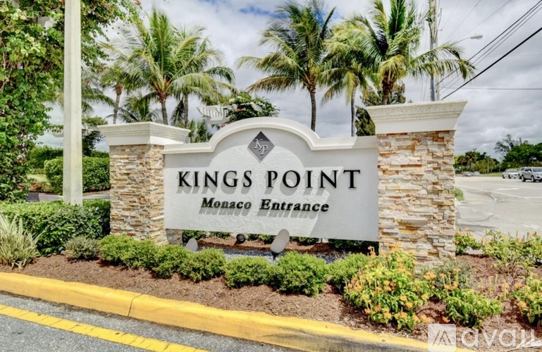 A sign that says Kings Point Monaco Entrance in front of some trees.