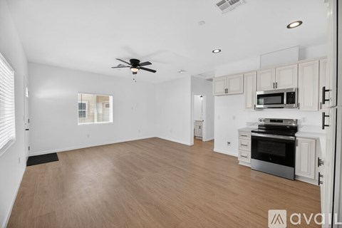 A spacious living room with a ceiling fan and a kitchen area with white cabinets and stainless steel appliances.