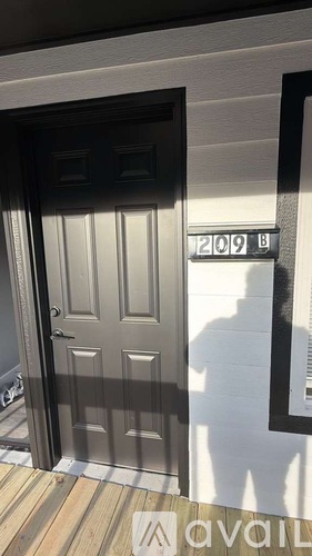 A black door with a silver handle is in front of a white wall with a number 209 on it.