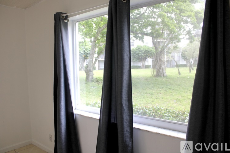 Black curtains hanging by a window with a view of a green lawn and trees outside.