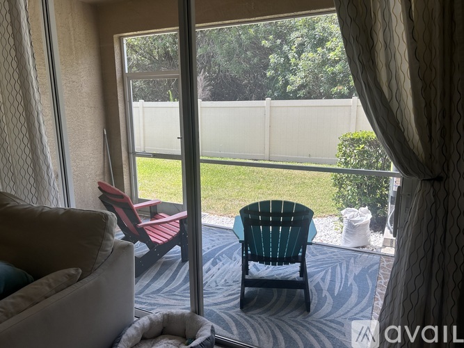 A patio with a chair and a couch with a view of a fence and trees.