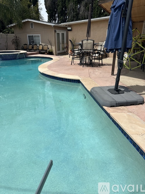A pool with a blue umbrella and chairs around it.