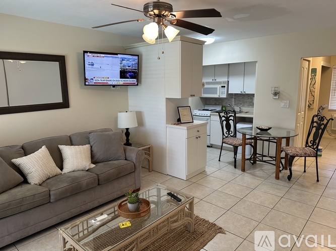 A living room with a grey couch, a glass coffee table, and a television mounted on the wall.
