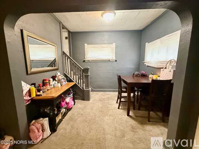 A room with a dining table and chairs, a staircase, and a mirror on the wall.