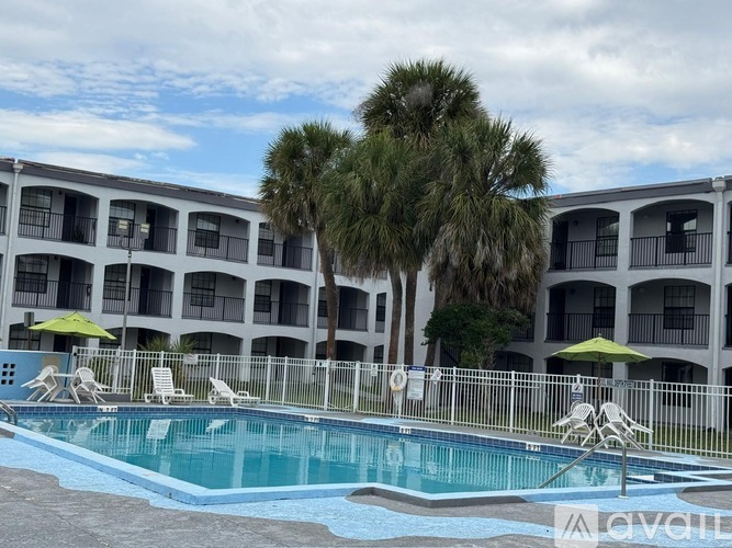 A pool area with chairs and umbrellas in front of a building.