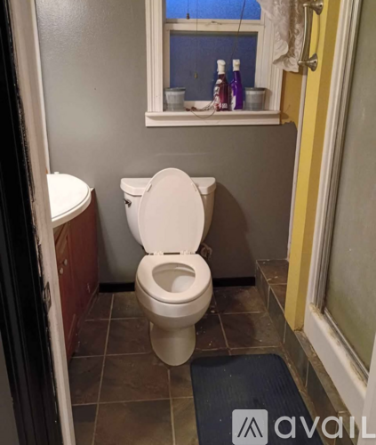 A white toilet in a small bathroom with a window above it.