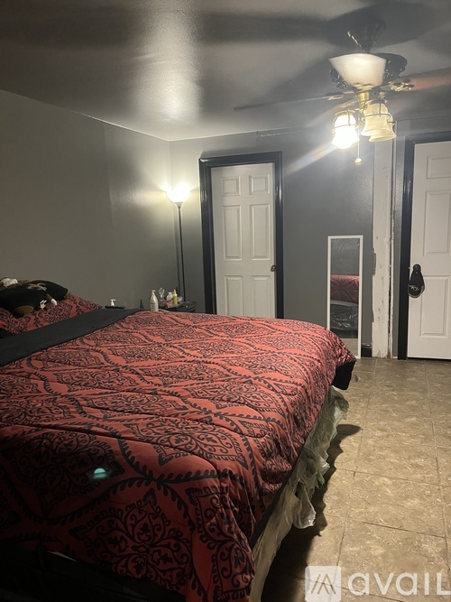 A bedroom with a red bedspread and a ceiling fan.