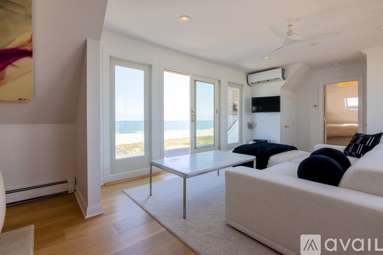 A living room with a white couch and a large window overlooking the beach.
