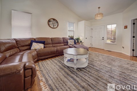 A living room with a brown leather couch and a round clock on the wall.