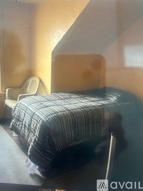 A bed with a striped comforter is in a room with a chair and a table.