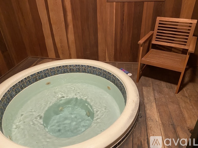 A hot tub sits in a wooden room with a chair to the side.