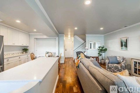 A well-lit, spacious living room with a grey sofa and a kitchen area with white cabinets.