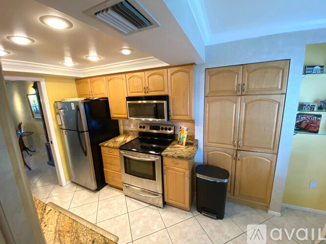 A kitchen with wooden cabinets and a black trash can.
