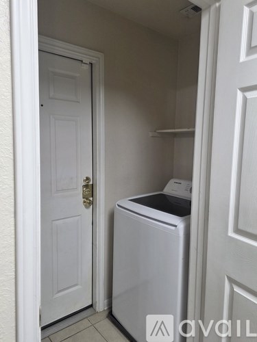 A white door with a gold handle is open to a small, white laundry room with a washer and dryer.