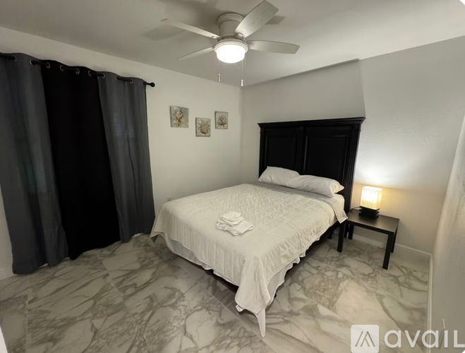A bedroom with a bed, a ceiling fan, and a nightstand with a lamp.