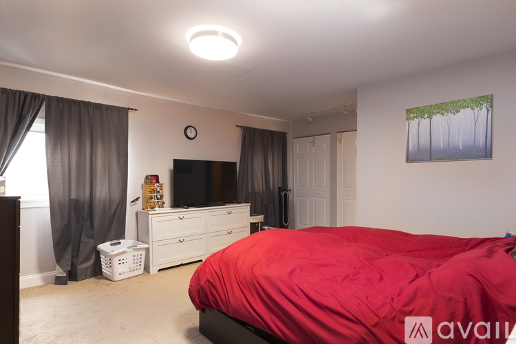 A bedroom with a red bedspread and a painting on the wall.
