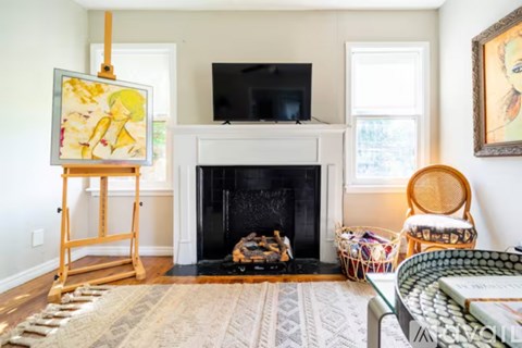 A living room with a fireplace, a painting on a stand, a television, a chair, and a coffee table.