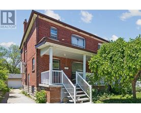 A red brick house with a white porch and a tree in front.
