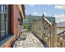 A wooden deck with a railing and a bench is in front of a building.