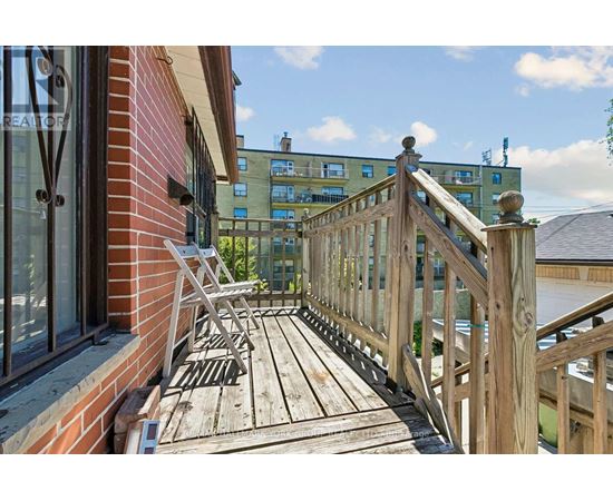 A wooden deck with a railing and a bench is in front of a building.
