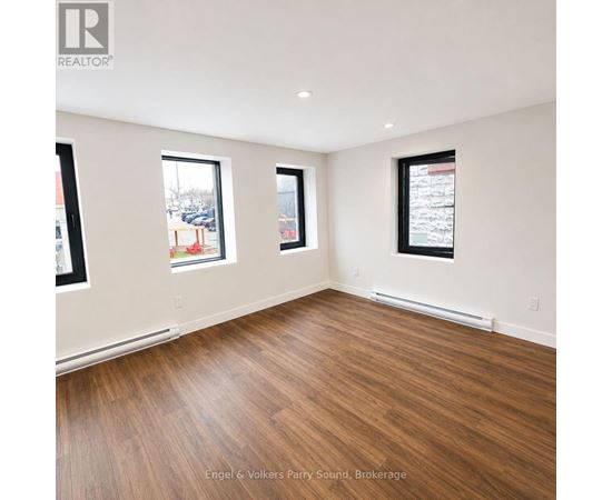 Empty room with wood flooring and two windows.