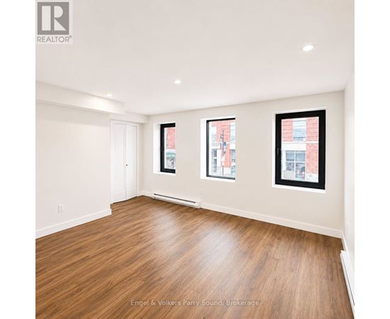 A spacious room with wooden flooring and three windows.