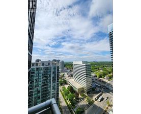 A cityscape with a mix of modern and older buildings, a clear sky with some clouds, and a road with moving vehicles.