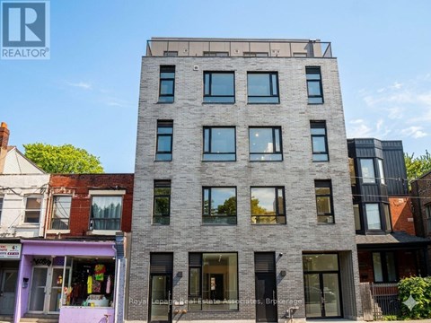 A tall grey building with many windows is in the middle of a street.