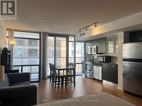 A modern kitchen with a dining table and chairs in the foreground and a view of a cityscape through the windows.