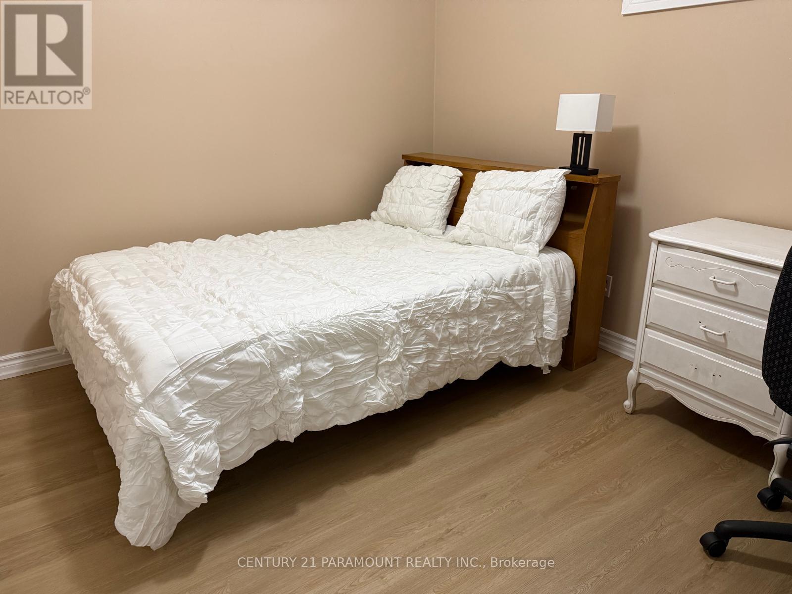 A white bed with a white comforter and two pillows sits in a room with a wooden headboard and a white nightstand with a lamp.