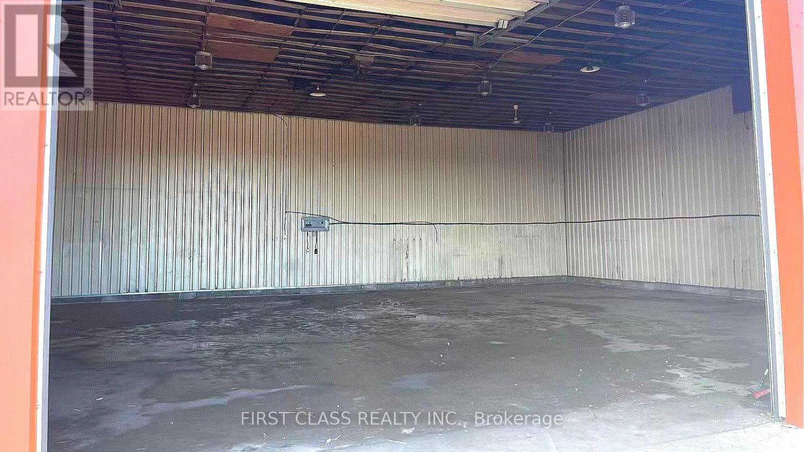A large empty room with a concrete floor and a wall covered in corrugated metal sheets.