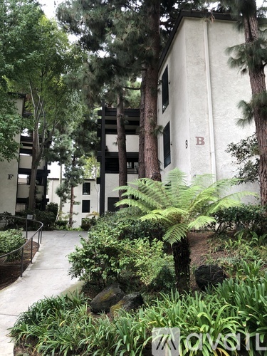 A white building with a red letter B on it is surrounded by trees and plants.