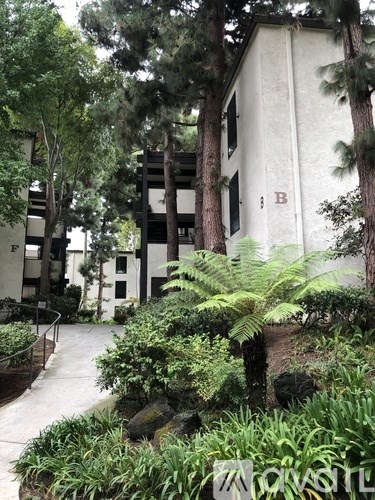 A white building with a red letter B on it is surrounded by trees and plants.