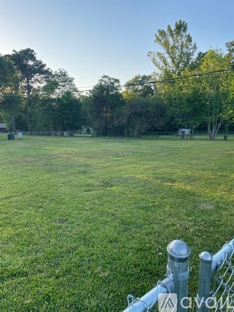 A grassy field with a fence in the foreground and trees in the background.