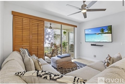 A living room with a couch, a fan, and a television displaying a beach scene.