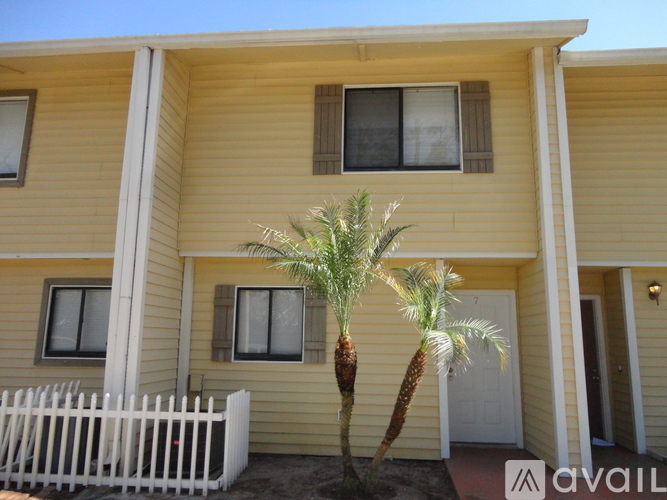 A yellow house with a white picket fence and a palm tree in front.