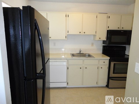 A black refrigerator stands in a kitchen with white cabinets and appliances.