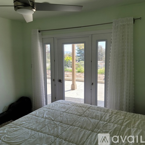 A bedroom with a large bed and a view of a fence and trees outside.
