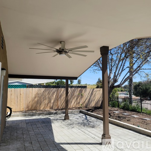 A patio with a ceiling fan and a view of a fence and trees.