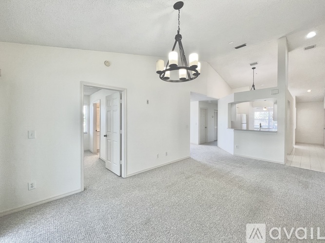 A spacious living room with a grey carpet and a chandelier hanging from the ceiling.