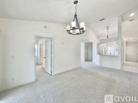 A spacious living room with a grey carpet and a chandelier hanging from the ceiling.