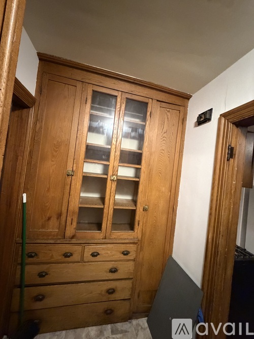 A wooden cabinet with glass doors and drawers is in the corner of a room.